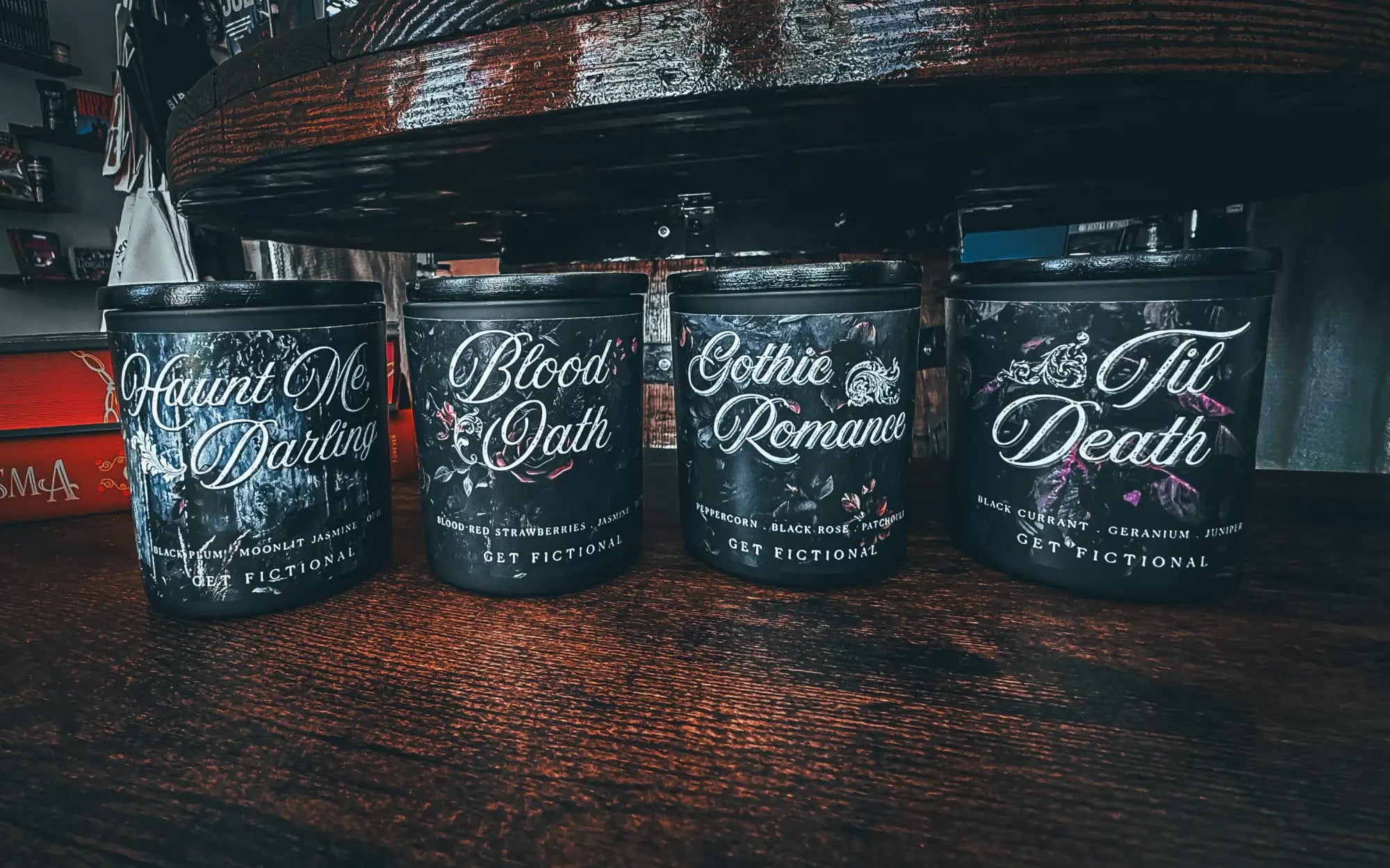 Four black scented candle jars with gothic-themed labels and white cursive text, each featuring a different fragrance name.