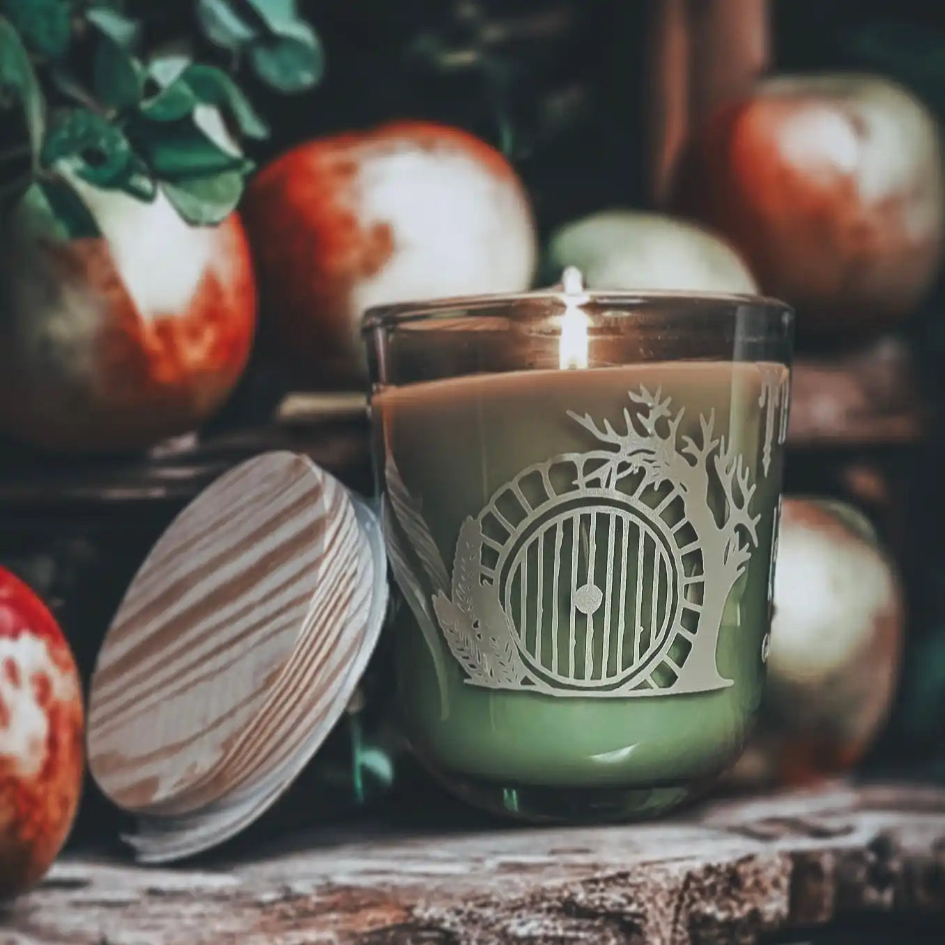 A green candle in a clear glass jar with a Hobbit door design and a wooden lid.